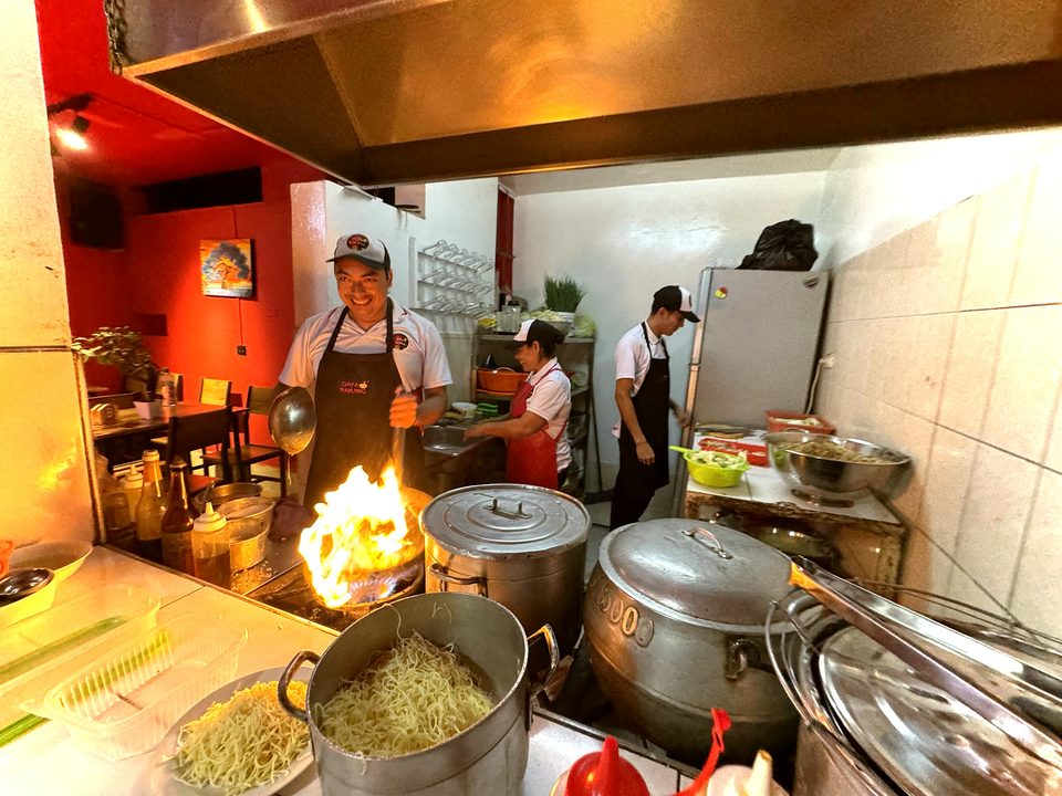 Los cocineros de Nanjing salteando al wok con fuego alto, en la cocina abierta del local